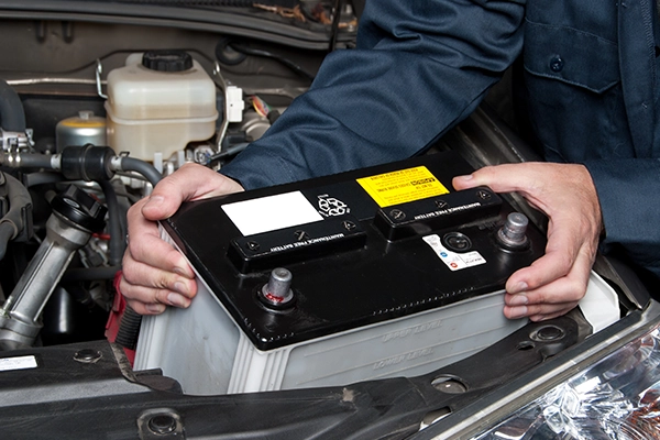Technician removing car battery from engine bay